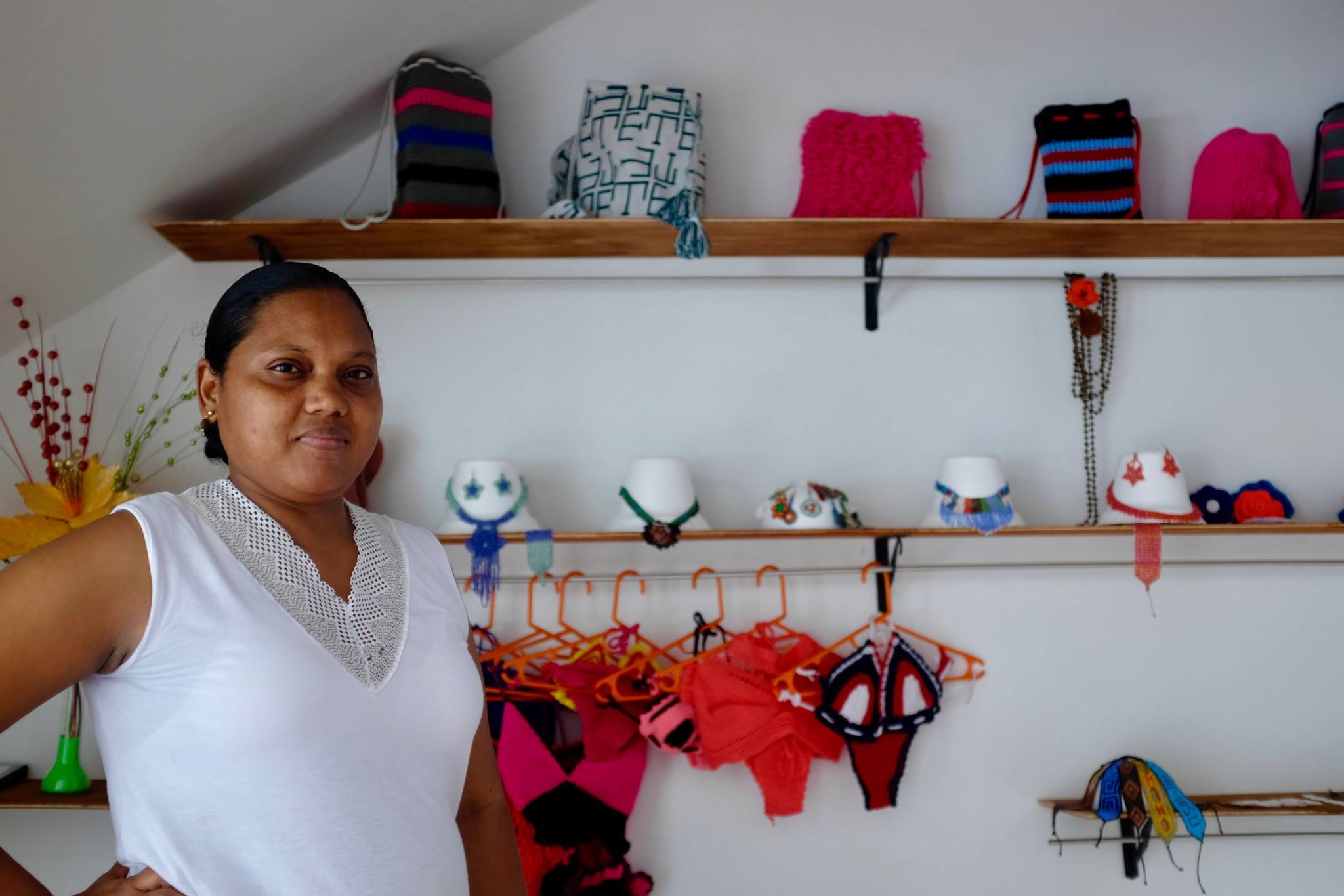 Une femme sourit devant un présentoir de sacs, bijoux et vêtements